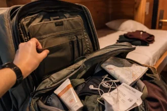 A traveler searching through an open backpack for a missing passport while sitting on a hostel bed abroad