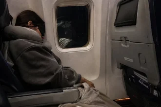 Passenger sleeping peacefully in economy class seat using a sleep mask and travel pillow