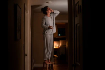 Tired homeowner standing on a stool at night trying to fix a chirping smoke alarm